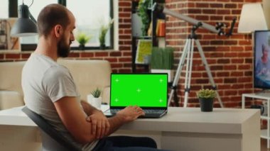 Ofis çalışanı, taşınabilir bilgisayardaki boş krom anahtar şablonunu inceleyip yeşil ekran ekranlı dizüstü bilgisayara bakıyor. İzole edilmiş arkaplan ve pc üzerindeki kopyalama alanı denetleniyor.