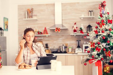 Torunum Noel günü kurabiye yiyor. Arka planda Noel ağacı var. Mutlu çocuk, Noel 'i kutlarken ve tablet bilgisayar izlerken büyükbabasından lezzetli kurabiyeler yiyor..