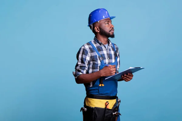 工事請負業者の肖像は すべての優れたタスクが完了していることを確認するために慎重に探して クリップボード上のタスクリストをチェックします 青を背景とした建設労働者 — ストック写真