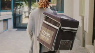 Kulaklıklı Afro-Amerikan kurye yürüyerek yemek getiriyor, müzik dinliyor ve bina kapısına doğru yürüyor. Paketten yemek paketi teslim etmeye hazırlanılıyor.