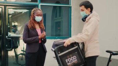 Yüz maskeli bir servis çalışanı ön kapıdaki Afro-Amerikan kadına yemek siparişi veriyor. Çoban köpeği 19 salgınında teslimat servisi. Kurye fast food restoranı paketini teslim ediyor..
