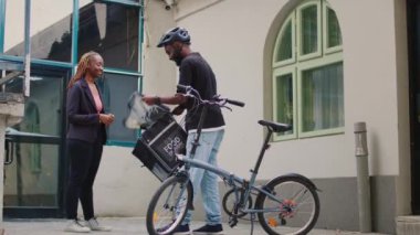 Erkek teslimat çalışanı kadın kadına fast food siparişi veriyor. Ön kapıda ofis yemeği servisi var. Kuryeden restoran siparişi alan kadın, elinde yemek paketi olan müşteri..