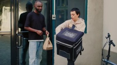Erkek müşteri restoranda yemek siparişi alıyor. Ukalaca davranıp ödemeyi NFC ile yapıyor. Yiyecek dağıtım servisi kuryesi kağıt torba içinde fast food veriyor, bağlantısız terminal..