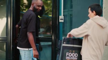 Afro-Amerikalı bir adam, Ukala 'yı terminalde ödeme yapmak için kullanıyor. Restoran yemeği için para ödüyor. Dişi teslimat kuryesi ön kapıya fast food paketi getiriyor. El kamerasıyla..