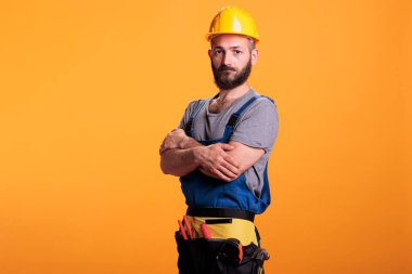 Mutlu tamirci marangoz. Üniforması yenileniyor ve şapkası stüdyoda kamera önünde poz veriyor. Profesyonel tamirci yenileme projesinde çalışmaya hazırlanıyor, usta bir zanaatkar..