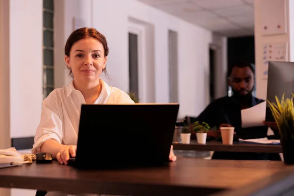 微笑着工作在公司笔记本电脑上的员工在合作空间的肖像 项目经理使用电脑 公司员工坐在工作岗位上 妇女在办公室工作到深夜 — 图库照片