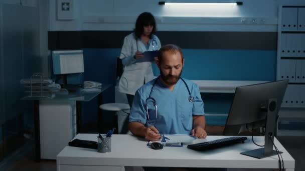 Ιατρικός Βοηθός Που Στέκεται Στο Γραφείο Του Νοσοκομείου Δουλεύοντας Νυχτερινή — Αρχείο Βίντεο