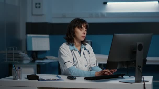 全科医生在医院办公室工作了好几个小时 分析病人在电脑上输入医疗报告的专业知识 医生计划进行医疗护理以治疗疾病 — 图库视频影像
