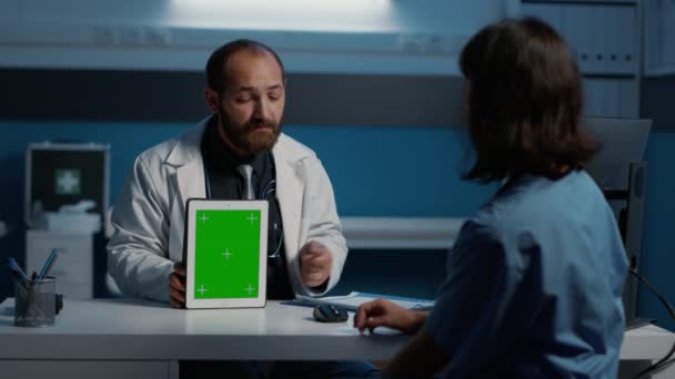 一般開業医は 緑色の画面のクロマキーが表示されたタブレットコンピュータを指して看護師に患者の病気の症状を説明します 病院で夜更かしをしている医療スタッフ — ストック動画