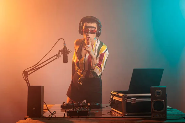 Disc jockey doing hush silence sign at turntables, showing mute and secrecy or privacy gesture with finger over lips. Woman advertising confidential symbol and producing music at mixer.
