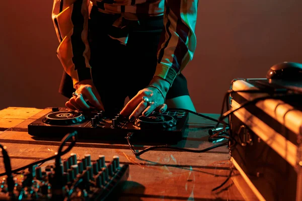 Woman performer mixing techno music on turntables, playing record mix sounds on audio dj instrument and stereo equipment. Enjoying nightclub party with stage production in studio.
