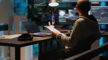 Yazılım geliştiricisi, pano kağıtları ve ekranlarındaki web verilerini analiz ediyor, dosyalardaki bilgileri karşılaştırıyor. Genç adam programlama dili kullanıyor ve geceleri yeni kullanıcı arayüzü kodluyor.