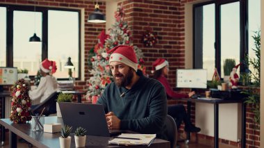 İnternetteki video konferans görüşmesinde konuşan erkek çalışan festival ofisinde Noel Baba şapkası takıyor. Yılbaşı tatilinde uzaktan telekonferans toplantısına katılmak, uzak konferans.