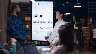 Şirketin yıllık yatırım kâr raporunu sunan çeşitli iş arkadaşları, birlikte çalışma alanında çalışan planlama satış stratejisi. Ofis çalışanları iş toplantısında, veri grafikleri dijital panoda