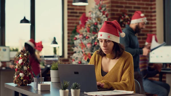 办公室工作人员计划在冬季节日期间用笔记本电脑启动项目 使用电脑在办公桌前操作 带着季节性装饰品和圣诞树在太空中工作的节日妇女 — 图库照片