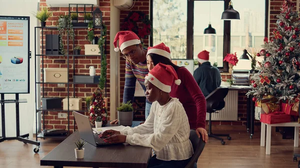不同的同事在笔记本电脑上集思广益 在装饰过节日的办公室里协同工作 在寒假期间与圣诞树和灯一起工作 庆祝节日 — 图库照片
