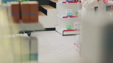 Uzman, engelli yaşlı bir adamın termometresiyle ateşi ölçüyor. Tekerlekli sandalye kullanıcısı sosyal hizmetliden yardım alıyor. Engelli bir müşteri eczacıyla konuşuyor. El kamerasıyla..