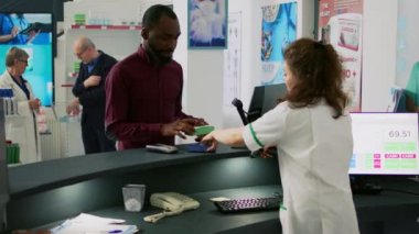Genç yetişkin ilaçların parasını NFC ile ödemek için cep telefonu kullanıyor, akıllı telefonu eczane tezgahının yakınında tutuyor. Erkek müşteri eczaneden ilaç ve vitamin alıyor..