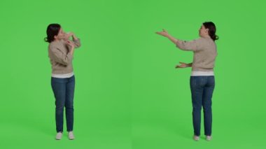 Stüdyodaki sunum ikonunu gösteren, reklam yapan ve kamerada örnek gösteren sıradan bir kadın. İzole edilmiş yeşil perde arkaplanı üzerinde poz veren, kendine güvenen kız reklam yapıyor..