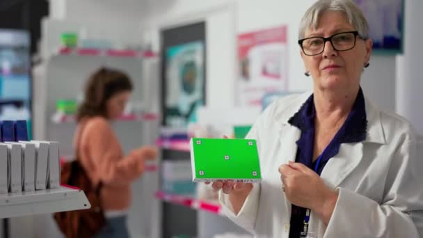 薬の箱に緑の画面を保持する製薬労働者 ドラッグストアで隔離されたモックアップテンプレートを示す女性専門家 空白のクロマキーを使用したシニア薬剤師コピースペースの背景 — ストック動画
