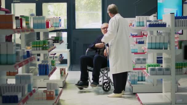 高齢者の車椅子ユーザーに循環器系薬瓶を与える薬剤師 慢性障害のある人は サポートを求めて 薬局で薬の治療を受ける障害のあるお客様 — ストック動画