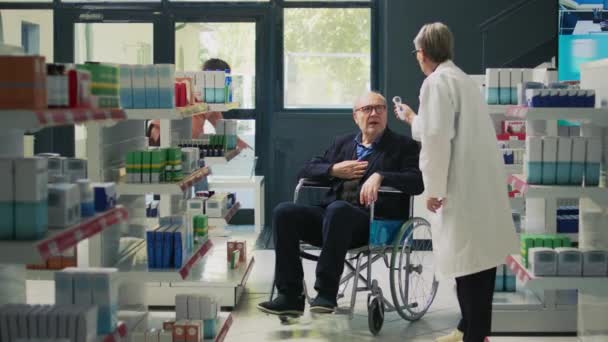 車椅子の人と温度計を使用して 障害のある人の温度を測定する医療専門家 障害者に優しい薬局で処方薬を購入する男性クライアント — ストック動画