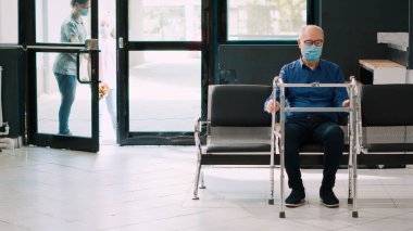 Anne ve kız tekerlekli sandalyedeki yaşlı bir hastayı görmeye gidiyorlar. Covid 19 salgını sırasında birini ziyaret ediyorlar. Yüzü maskeli insanlar klinikteki yaşlı kadınla konuşmak için hastane lobisine giriyorlar. El kamerasıyla..