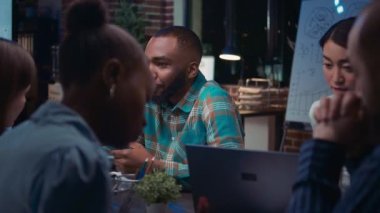 Gülümseyen Afro-Amerikan bir çalışan iş dünyasının portresiyle tanışıyor, yavaş çekim orta ölçekli. Kameraya bakan adam, çeşitli iş arkadaşları beyin fırtınası, planlama stratejisi