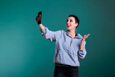 Çevrimiçi video görüşmesi sırasında uzaktan arkadaşıyla konuşurken gülümseyen neşeli beyaz kadın, izole bir geçmişe sahip stüdyoda duruyor. Kadın video konferansında takımla sohbet ediyor.