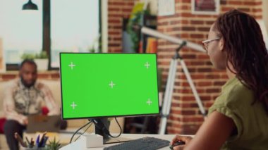 Bilgisayarda yeşil ekrana bakan genç bir iş kadını, izole bir şablonla evden uzaktan çalışıyor. Boş model kopyalanmış ekran pc ile krom anahtar görüntüsü kullanan kadın.