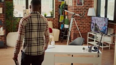 Bilgisayarla serbest çalışmak için masada oturan genç yetişkin, veri ve bilgilerle şirket raporu oluşturmak için çevrimiçi ağı kullanıyor. Şirket çalışanı oturma odasında uzaktan kumanda yapıyor..