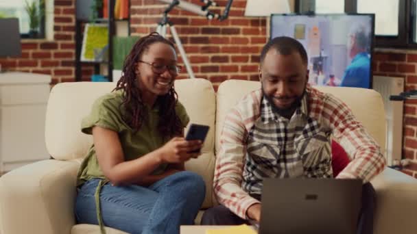 男人和女人在家里浏览智能手机和笔记本电脑 享受互联网上的休闲活动 夫妻在家里一起使用现代设备的时候 开心地笑着 — 图库视频影像