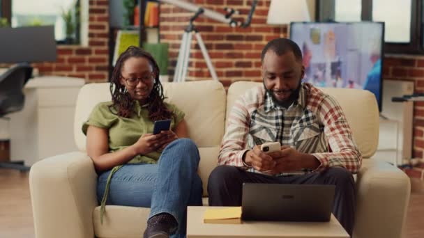African American Ζευγάρι Χρησιμοποιώντας Smartphones Μαζί Στον Καναπέ Περιήγηση Στο — Αρχείο Βίντεο