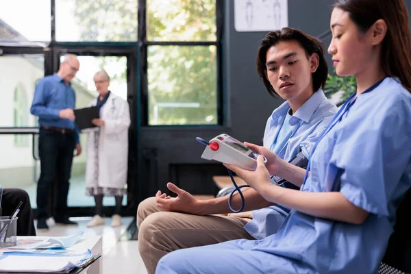 患者の血圧や高血圧を測定するアジアの医療アシスタントは 病院の待合室で計測器で 看護師は心臓パルスをチェックし 心臓検査を行う — ストック写真