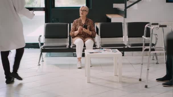 男性の健康の専門家の相談室に老婦人を取って 高齢者の患者は病院の待合室に座っている 一般開業医と面会の約束をした者 — ストック動画