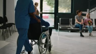 Hemşire, tekerlekli sandalyedeki adama klinikte ailesiyle buluşması için yardım ediyor. Hastanedeki kronik bozukluklarla ilgilenen yaşlı bir hasta. Anne ve çocuk bekleme odasını ziyaret ediyor..