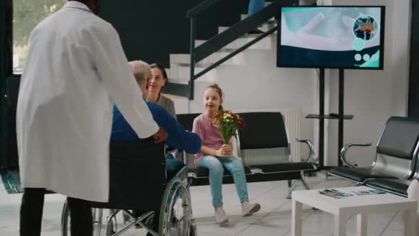 高齢者の健康を検査した後 待合室のロビーで車椅子を使用して歩いて感じている 老人は身体障害が治り 女性や小さな子供と話す — ストック動画