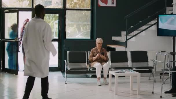 男医生与老年妇女一起参加检查预约 带病人到内阁 并开始咨询 在诊所与病人进行体格检查的年轻人 — 图库视频影像