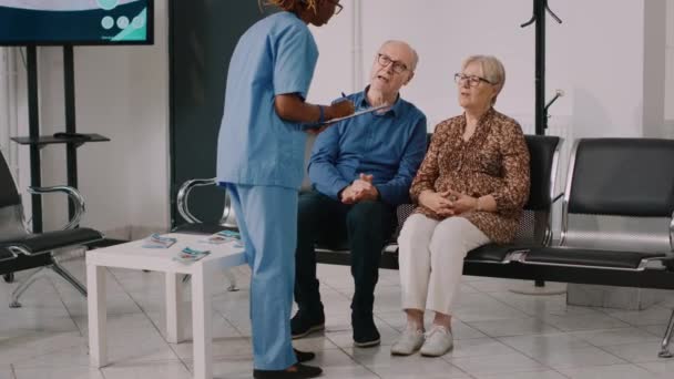 Αφροαμερικανή Νοσοκόμα Που Μιλάει Ηλικιωμένους Στην Αίθουσα Αναμονής Περιμένοντας Παρακολουθήσει — Αρχείο Βίντεο