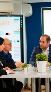 Genç adam şirket lideri iş konferansı için çeşitli takımların gelmesini bekliyor. Geniş bir masada oturuyorlar. İdari Direktör çok ırklı insanlara brifing vererek, mali raporların başlatılmasını açıklıyor