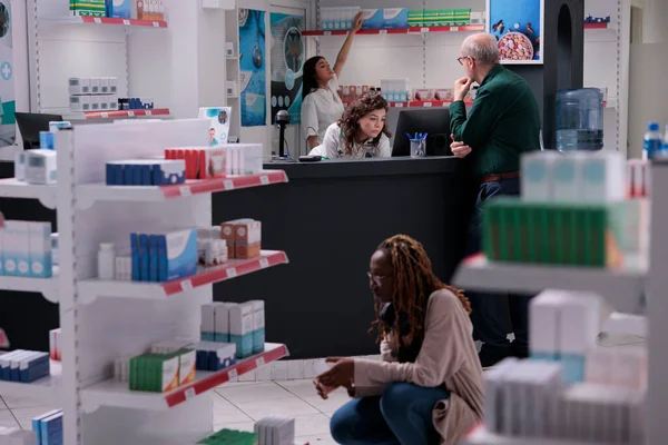Customer asking pharmacist for medical advice discussing about pills prescription during consultation in pharmacy. Drugstore shelves full with drugs, vitamin and supplements. Medicine support