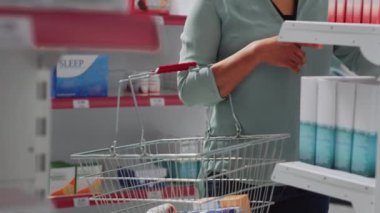 Asyalı müşteri eczaneden ilaç ve vitamin almak için sepetine ilaç koyuyor. Raflardaki ilaç ve ilaç paketlerini kontrol eden bir kadın. El kamerasıyla..