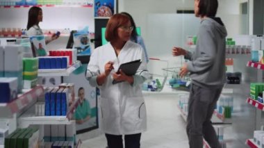 Tıbbi danışman ilaç envanteri yapmak için dijital cihaz kullanıyor eczane raflarındaki ilaç ürünlerini analiz ediyor. Eczacı olarak çalışan kadın eczane stoklarına bakıyor..