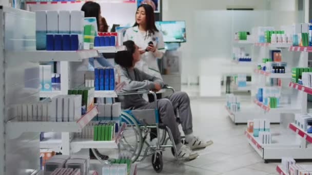 年轻的轮椅使用者与药剂师谈论药物 询问处方药或药物 在药房接受补充剂和维生素的残疾人和护理人员 — 图库视频影像