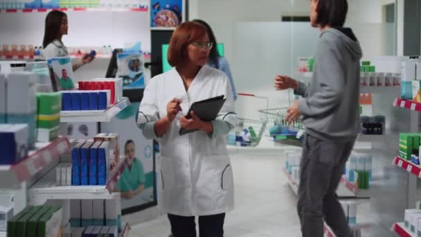 医療コンサルタントは 医薬品在庫を行うためにデジタルガジェットを使用して ドラッグストアの棚に医薬品を分析します 薬局用品を見る薬剤師として働く女性 — ストック動画