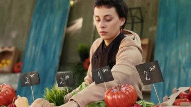 Önlüklü başarılı bir çiftçi çiftçi pazarı işletiyor, tüketicilere mevsimsel organik ürünler satıyor. Çapraz kollarla poz veren ve kameraya bakan kadın manav. El kamerasıyla..