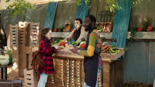 年轻的男性卖主在农贸市场上展示天然生物产品并与客户交谈 本地种植有机水果及蔬菜的街市 街市档位 — 图库视频影像