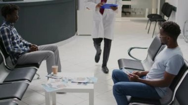 Hastane resepsiyonunda erkek hastayla istişare yapan uzman bir doktor muayene sonuçları ve tedavi hakkında konuşuyor. Tıbbi form kağıtları üzerinde notlar gösteren pratisyen hekim.