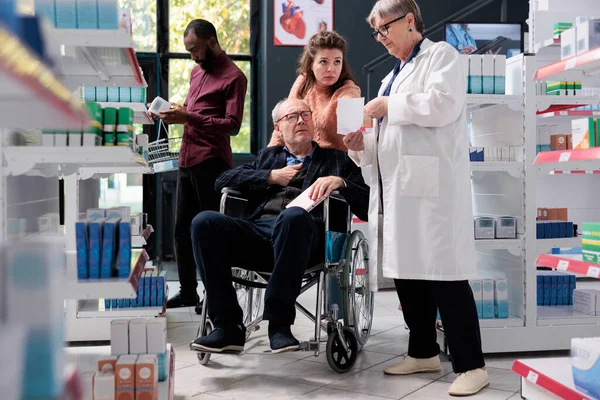 Elderly Drugstore Worker Discussing Health Care Treatment Disabled Client Reading — Stock Photo, Image