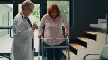 Yaşlı doktor, klinikte yürümeye çalışan, fizyoterapi randevusuna katılan yaralı hastalara destek veriyor. Bacak kırığı, ağrı ve rehabilitasyonla uğraşıyoruz..